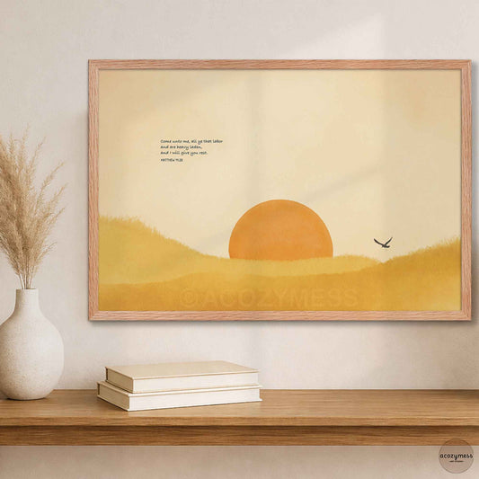 Oak framed Bible verse sun landscape print above a wooden shelf with books and a white vase of dried grass