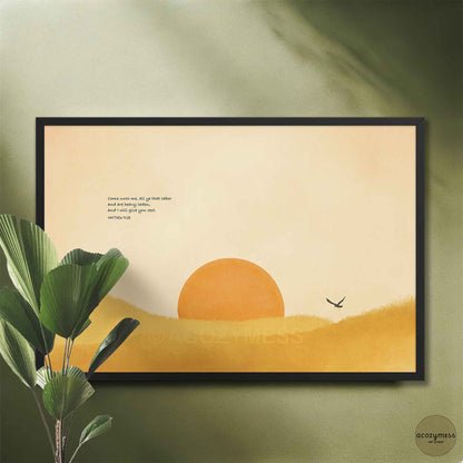 Black framed Matthew 11:28 Bible verse art with an orange sun on a sage green wall beside a leafy plant