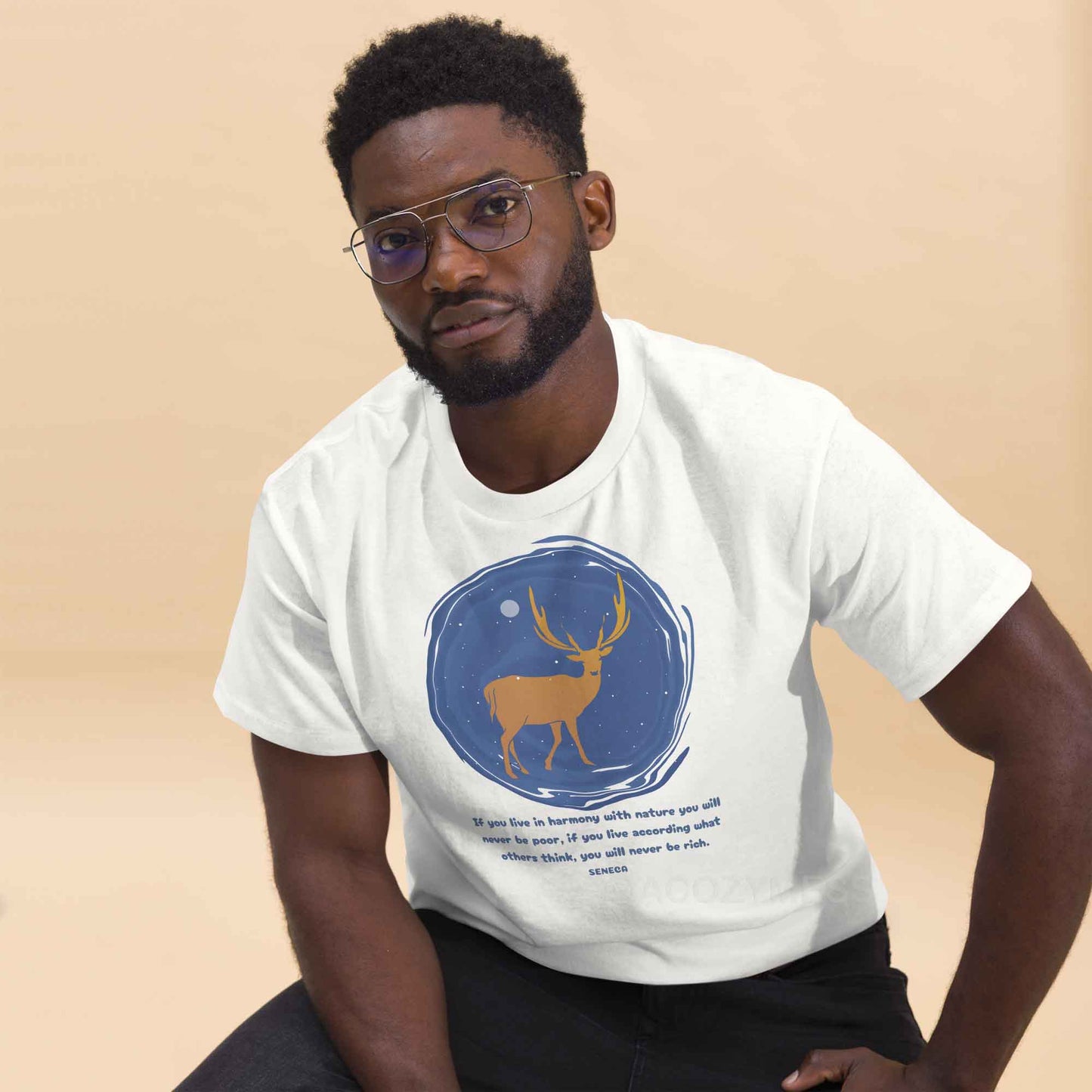  A white T-shirt featuring a minimalist design of a majestic deer standing under a starry night sky, accompanied by a quote from Seneca: If you live in harmony with nature, you will never be poor. If you live according to what others think, you will never be rich.