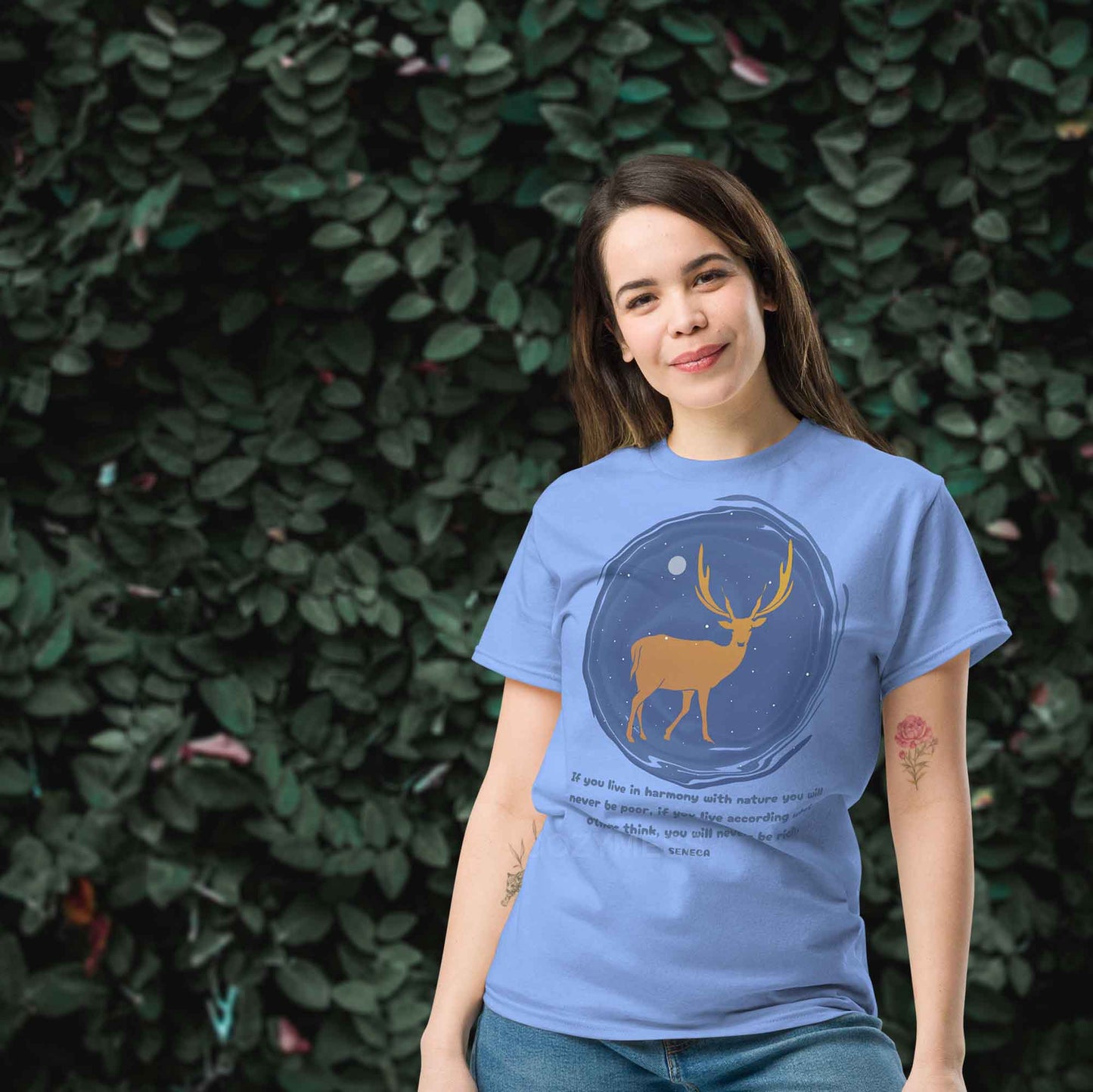  A carolina blue T-shirt featuring a minimalist design of a majestic deer standing under a starry night sky, accompanied by a quote from Seneca: If you live in harmony with nature, you will never be poor. If you live according to what others think, you will never be rich.