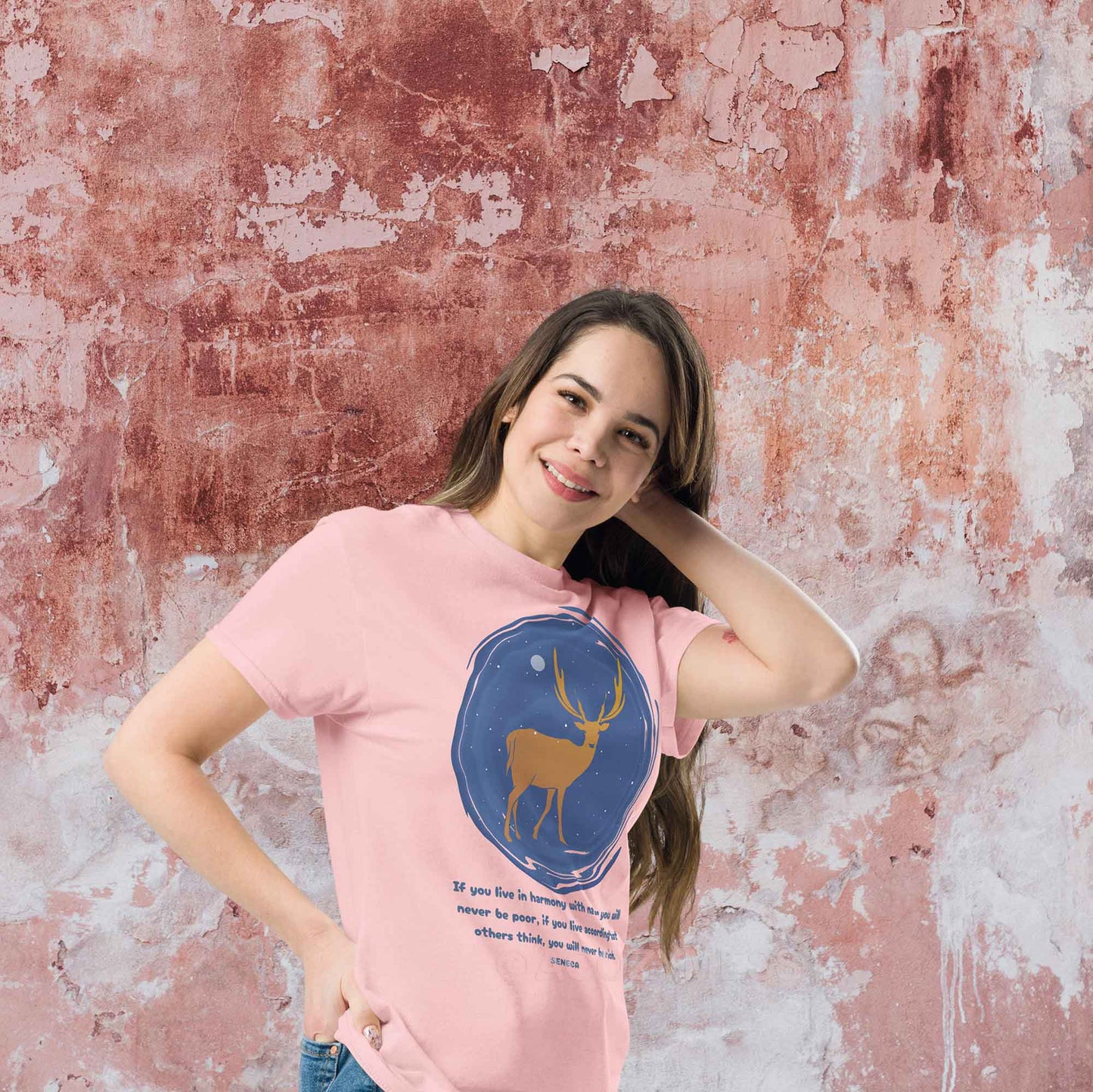  A light pink T-shirt featuring a minimalist design of a majestic deer standing under a starry night sky, accompanied by a quote from Seneca: If you live in harmony with nature, you will never be poor. If you live according to what others think, you will never be rich.