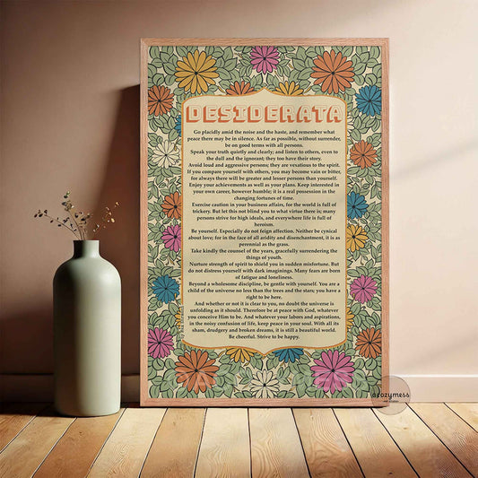 A framed decorative print with a colorful retro floral border and a Desiderata Poem leaning against a beige wall on a wood floor beside a small white vase.