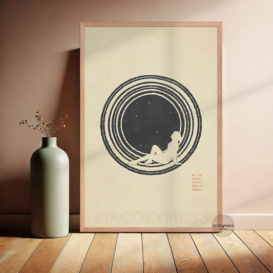 A minimalist Stoic art poster framed in a light oak wood frame, leaning against a wall on a light hardwood floor. The artwork features a clean, stylized illustration of a person gazing up at a minimalist star-filled sky against a warm beige background. Elegant, vertical typography reads: "ALL THE PRESENT IS A POINT IN ETERNITY. Marcus Aurelius."