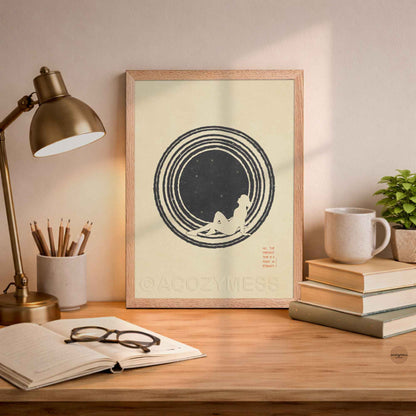 An oakwood framed  minimalist philosophy poster featuring a clean illustration of a lone figure stargazing beneath a vast, starry sky. The artwork is framed in a sleek border, displaying sharp typography with the Marcus Aurelius quote on present moment leaning on a desk .