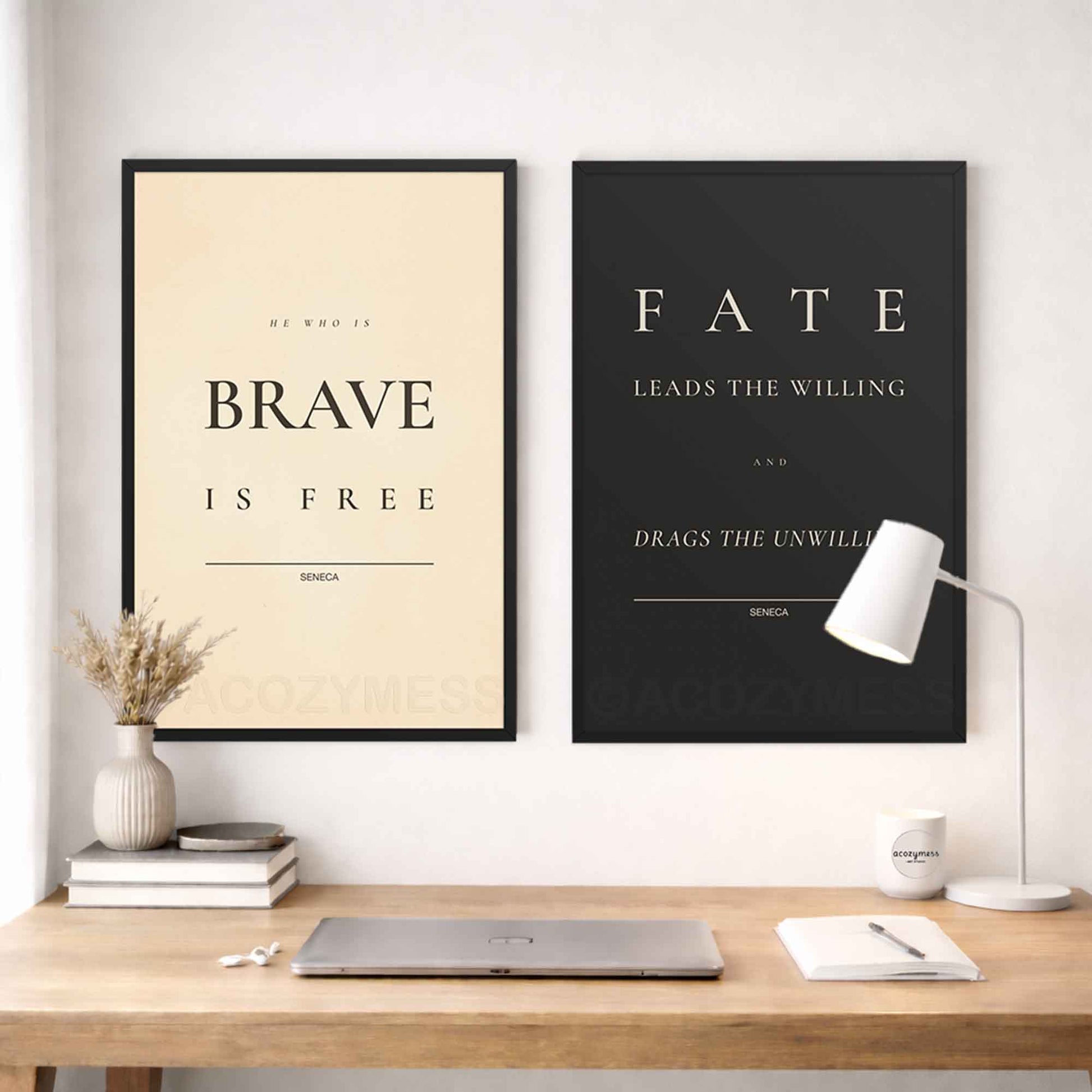 Two black framed stoic quotes on a wall above a desk with a lamp and books.