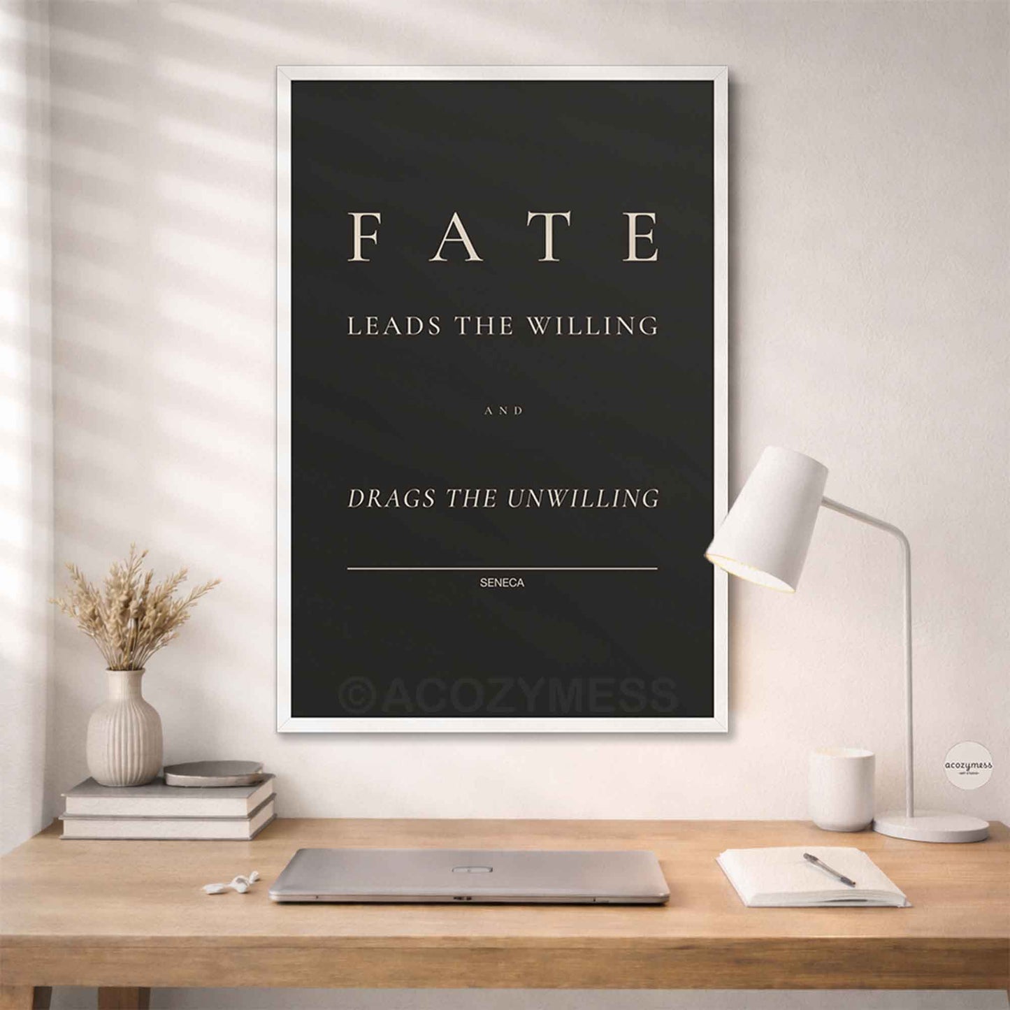 White Framed poster with 'Fate leads the willing and drags the unwilling' quote by Seneca on a wall above a desk.