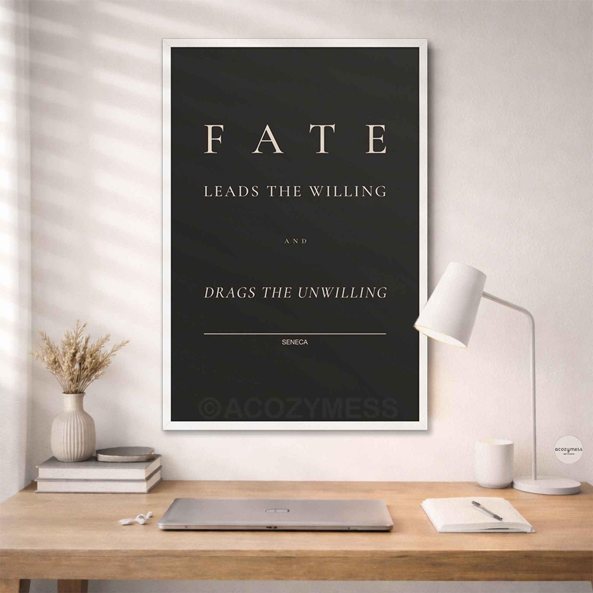 White Framed poster with 'Fate leads the willing and drags the unwilling' quote by Seneca on a wall above a desk.