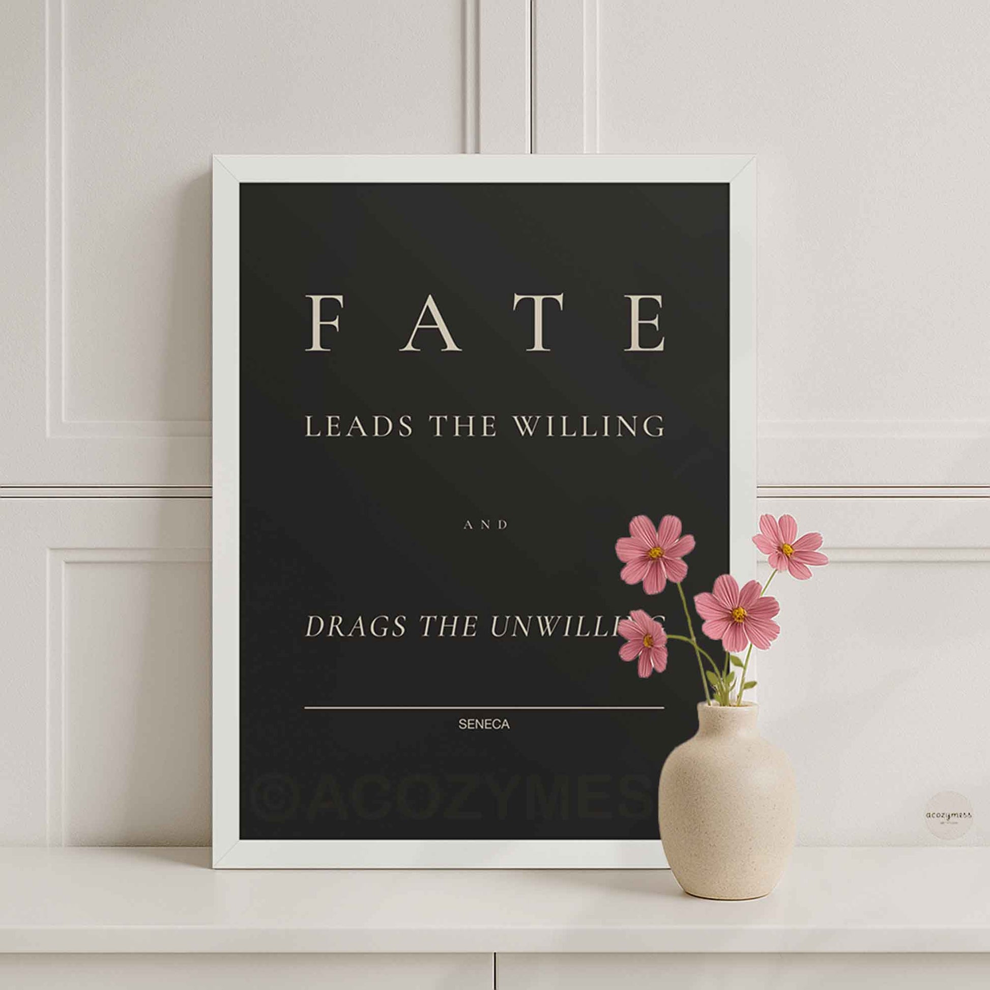 White Framed poster with Seneca quote 'Fate leads the willing and drags the unwilling' on a white wall with a vase of pink flowers.