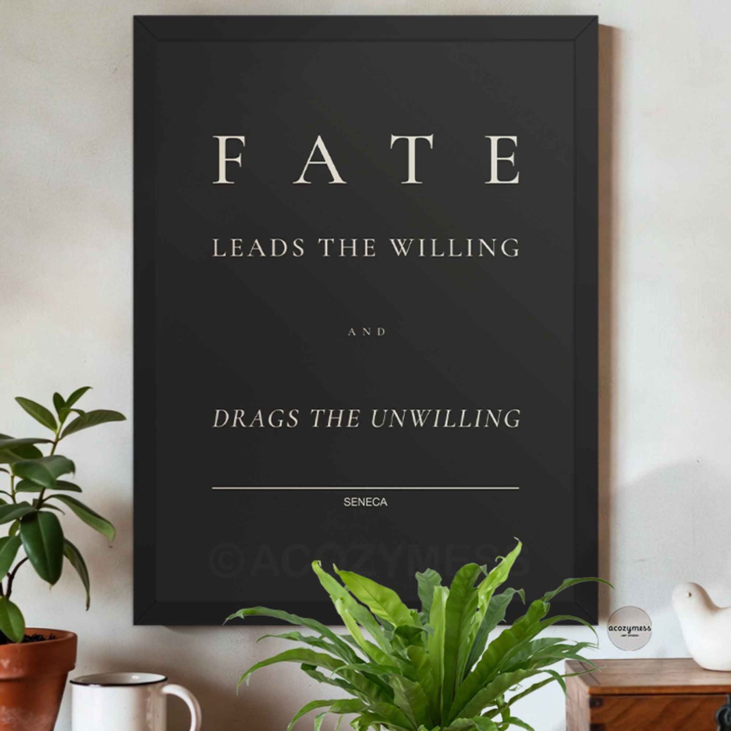 Framed poster with Seneca quote 'Fate leads the willing and drags the unwilling' on a wall with plants and decor.