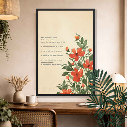 A Black framed art print featuring a botanical illustration of red-orange flowers and green leaves on a cream background, with a quote printed on the left side. The frame is displayed on a wall above a wooden console table.