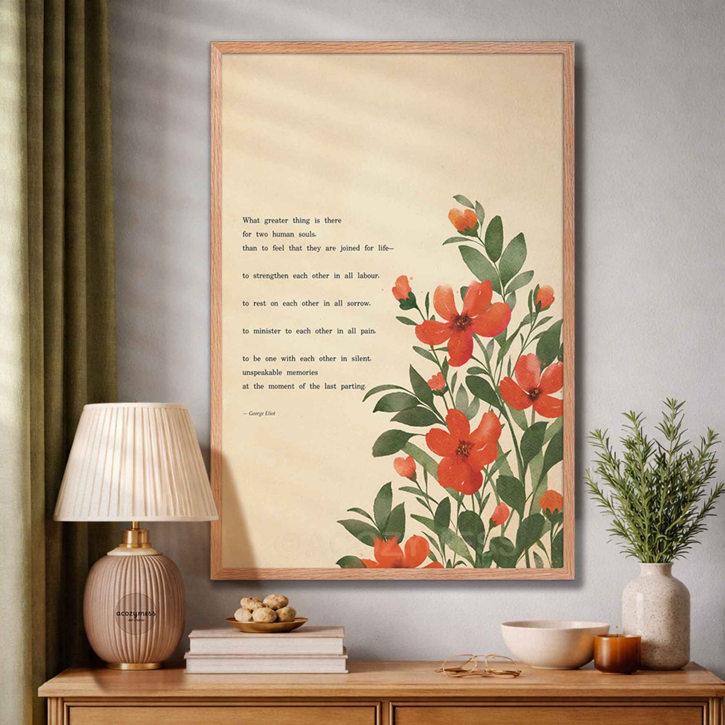 A framed art print featuring a quote by George Eliot about love and vibrant red flowers with green leaves on a beige background, styled in a warm, modern living room setting on a wooden console table.