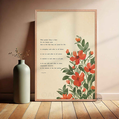 A framed art print featuring a quote by George Eliot about love and red flowers, styled leaning against a wall on a wooden floor.