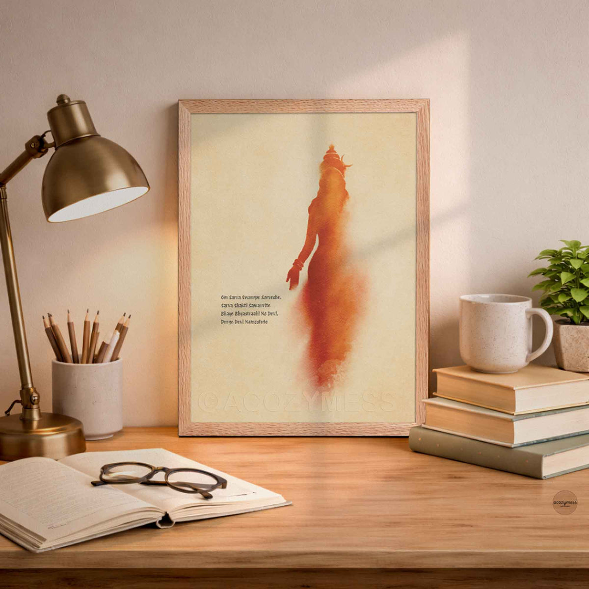 A framed art print featuring a red  silhouette of maa durga on a cream background with durga mantra, styled on a wooden desk.