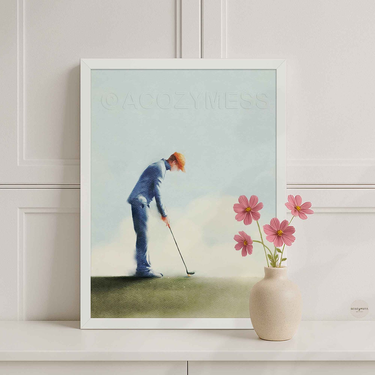White Framed artwork of a golfer on a golf course with a vase of flowers on a shelf.