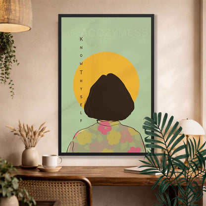 A black framed art print featuring a minimalist illustration of a person with a short dark bob haircut seen from behind, standing in front of a yellow sun on a pale green background. 