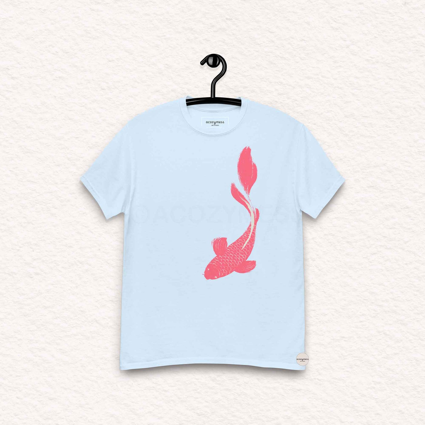 Light blue t-shirt with a pink fish design on a hanger against a light background