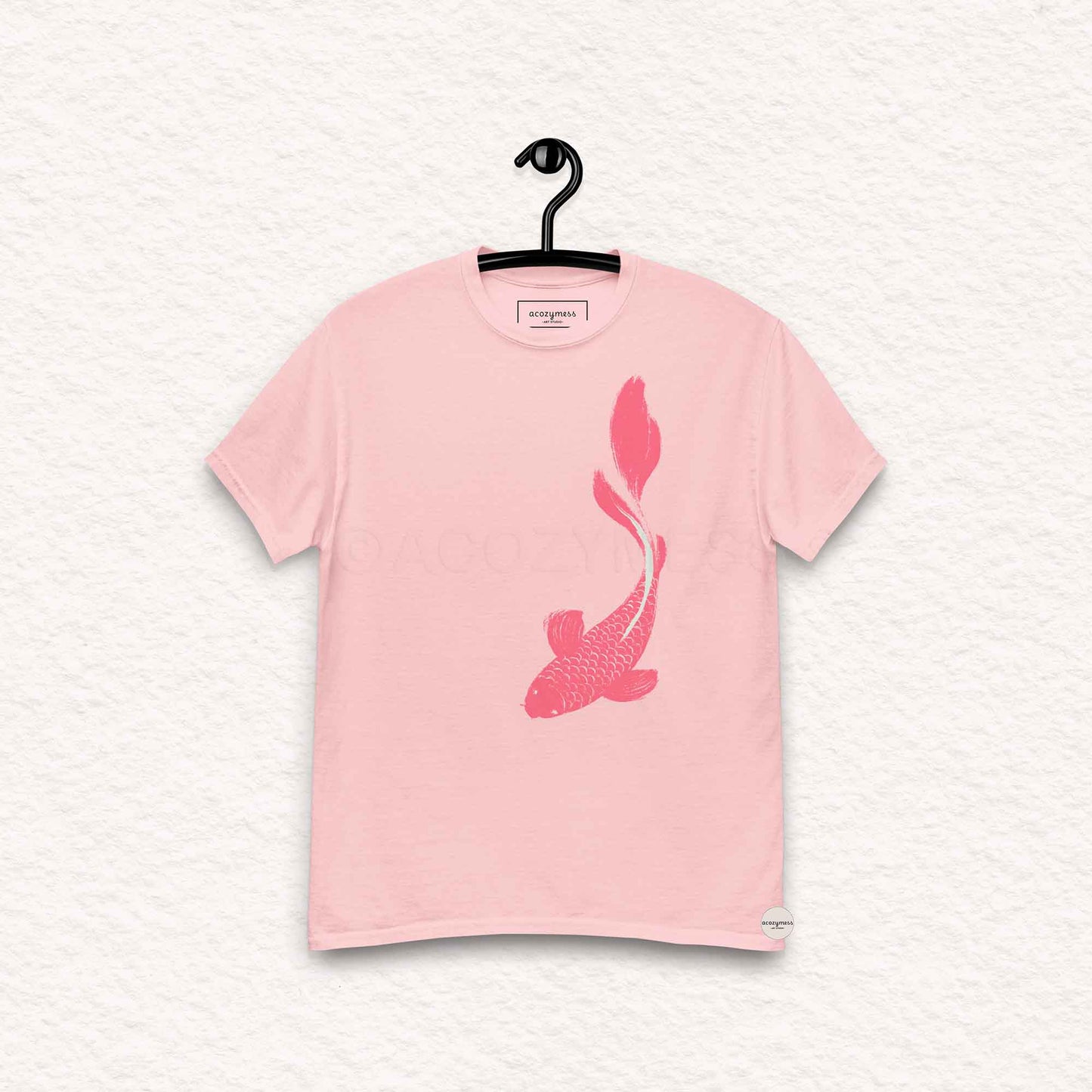Pink t-shirt with a fish design on a hanger against a light gray background
