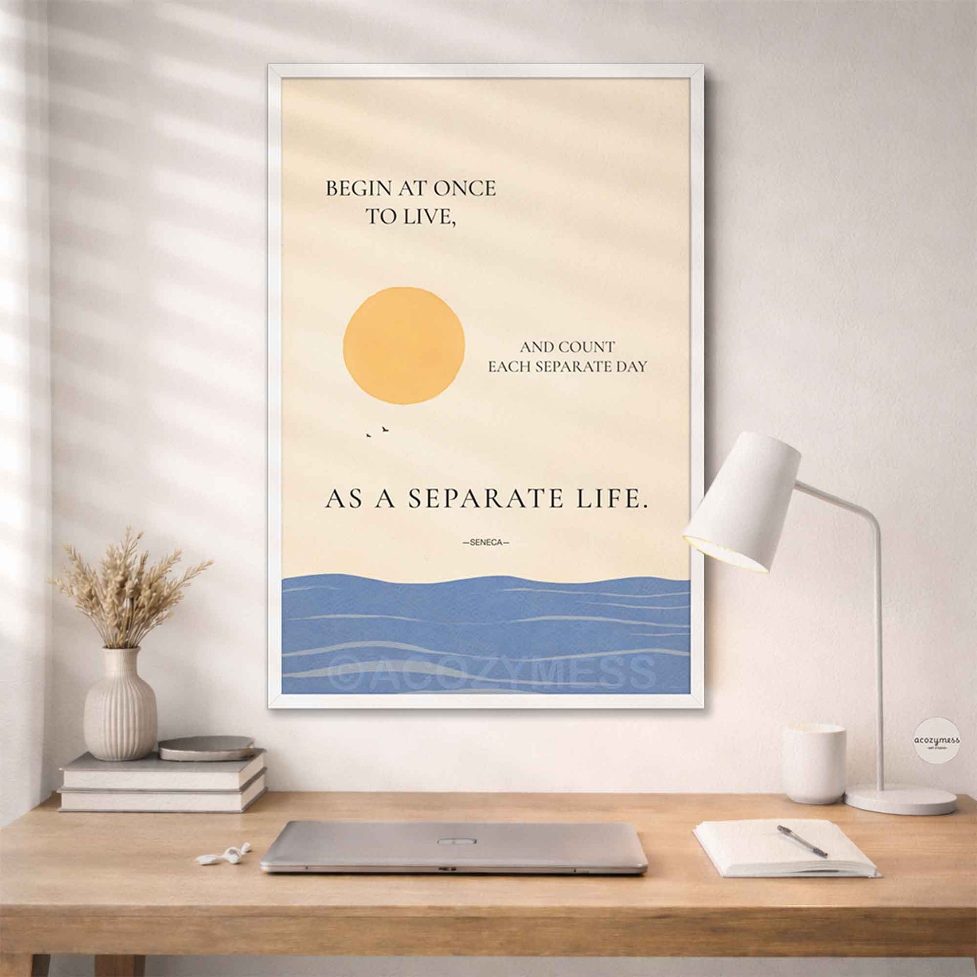 Seneca Stoic quote wall art in white frame on beige background with sun and sea on a wall above a desk.