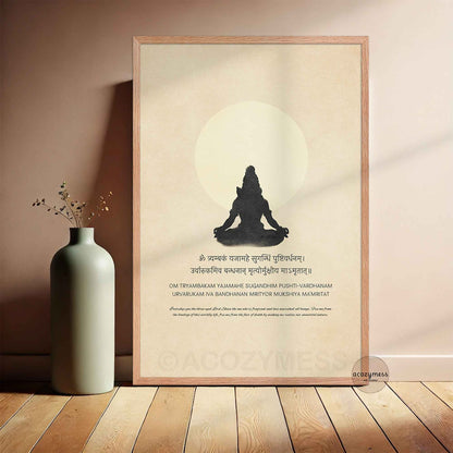 A minimalist spiritual art poster framed in a light oak wood frame, leaning against a wall. The artwork features a deep silhouette of Lord Shiva in a meditation pose in front of a full moon on a warm beige background, surrounded by the Maha Mrityunjaya Mantra and its English translation.
