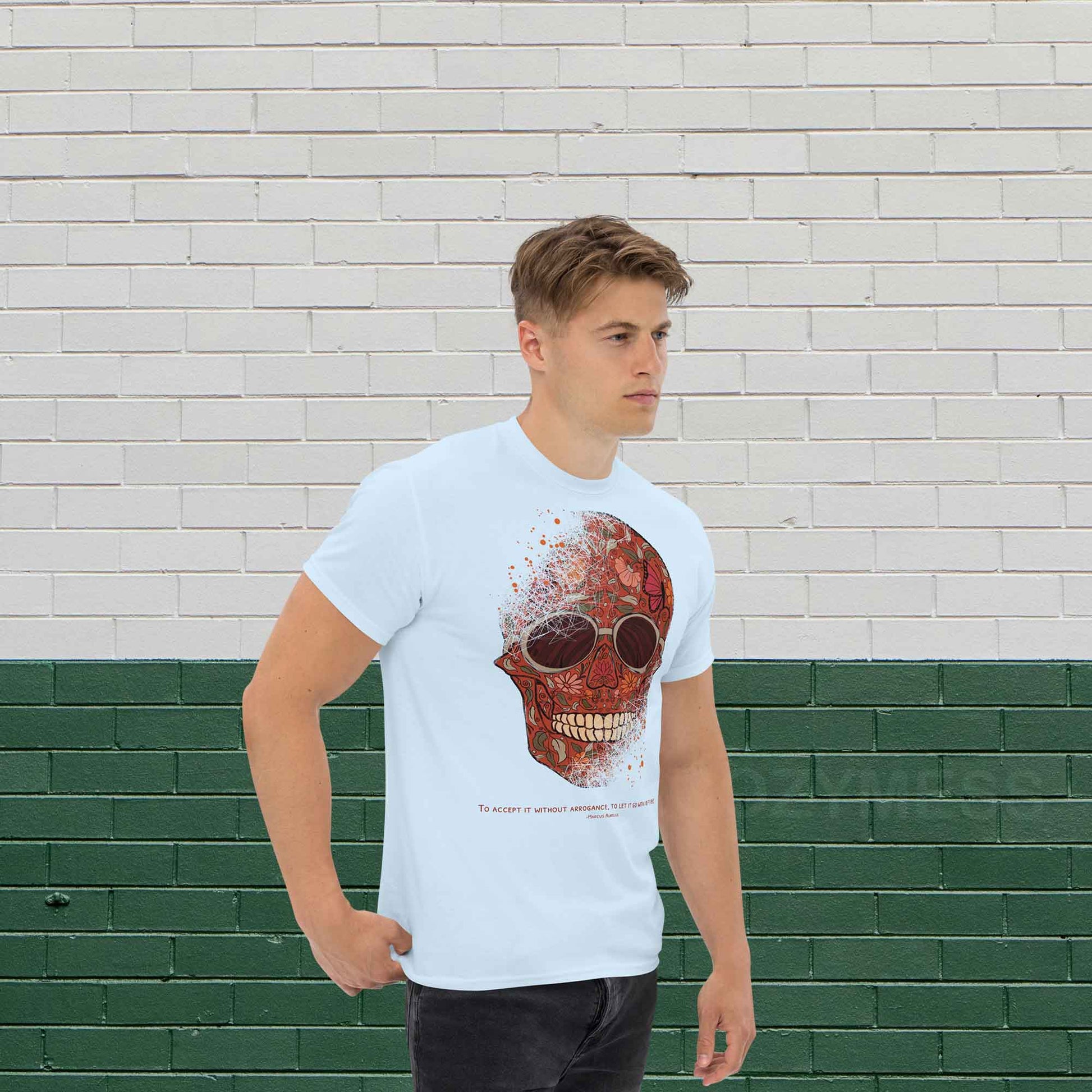 A man wearing light blue color T-shirt featuring a detailed skull and floral design, paired with a Marcus Aurelius quote: "To accept it without arrogance, to let it go with indifference." The artwork symbolizes memento mori and Stoic philosophy, blending mortality with beauty.