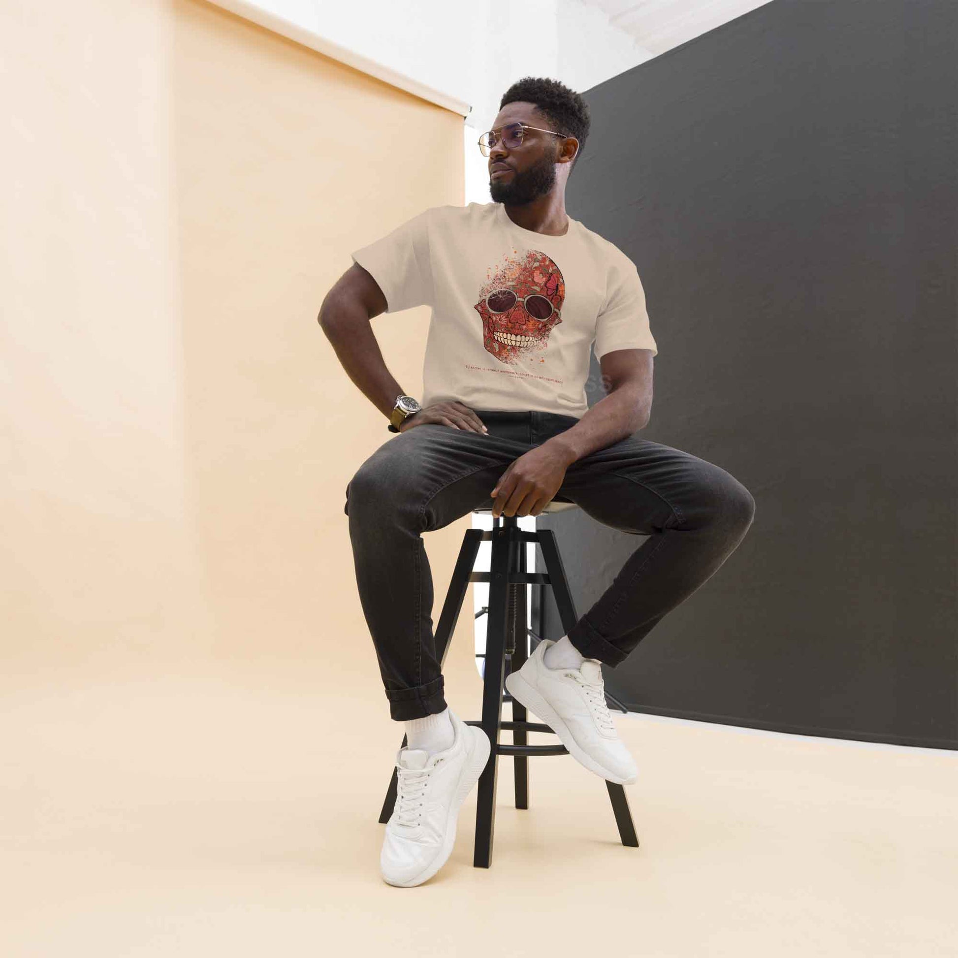 A man wearing sand color T-shirt featuring a detailed skull and floral design, paired with a Marcus Aurelius quote: "To accept it without arrogance, to let it go with indifference." The artwork symbolizes memento mori and Stoic philosophy, blending mortality with beauty.