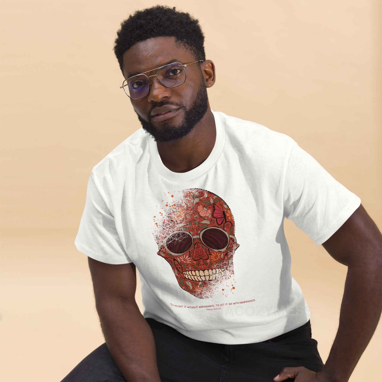 A white Tee featuring a detailed skull and floral design, paired with a Marcus Aurelius quote: "To accept it without arrogance, to let it go with indifference." The artwork symbolizes memento mori and Stoic philosophy, blending mortality with beauty.