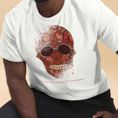 A white Tee featuring a detailed skull and floral design, paired with a Marcus Aurelius quote: "To accept it without arrogance, to let it go with indifference." The artwork symbolizes memento mori and Stoic philosophy, blending mortality with beauty.
