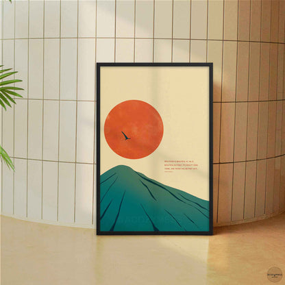 A framed minimalist art print leaning against a beige tiled wall on a light floor. The print features a stylized teal mountain and a large orange sun on a cream background, with small text and a bird silhouette.