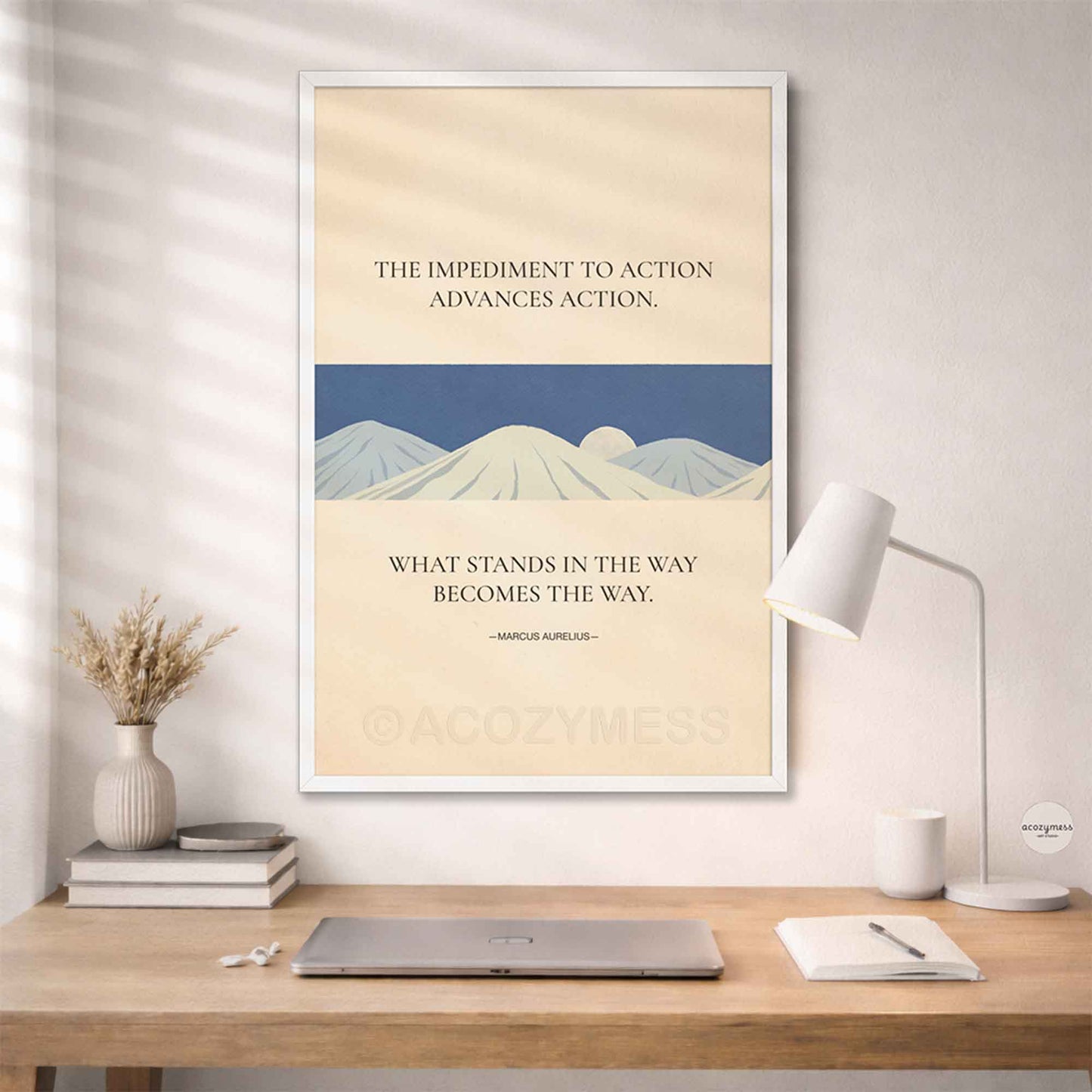 White Framed motivational poster with mountain design and quote on a wall above a desk.