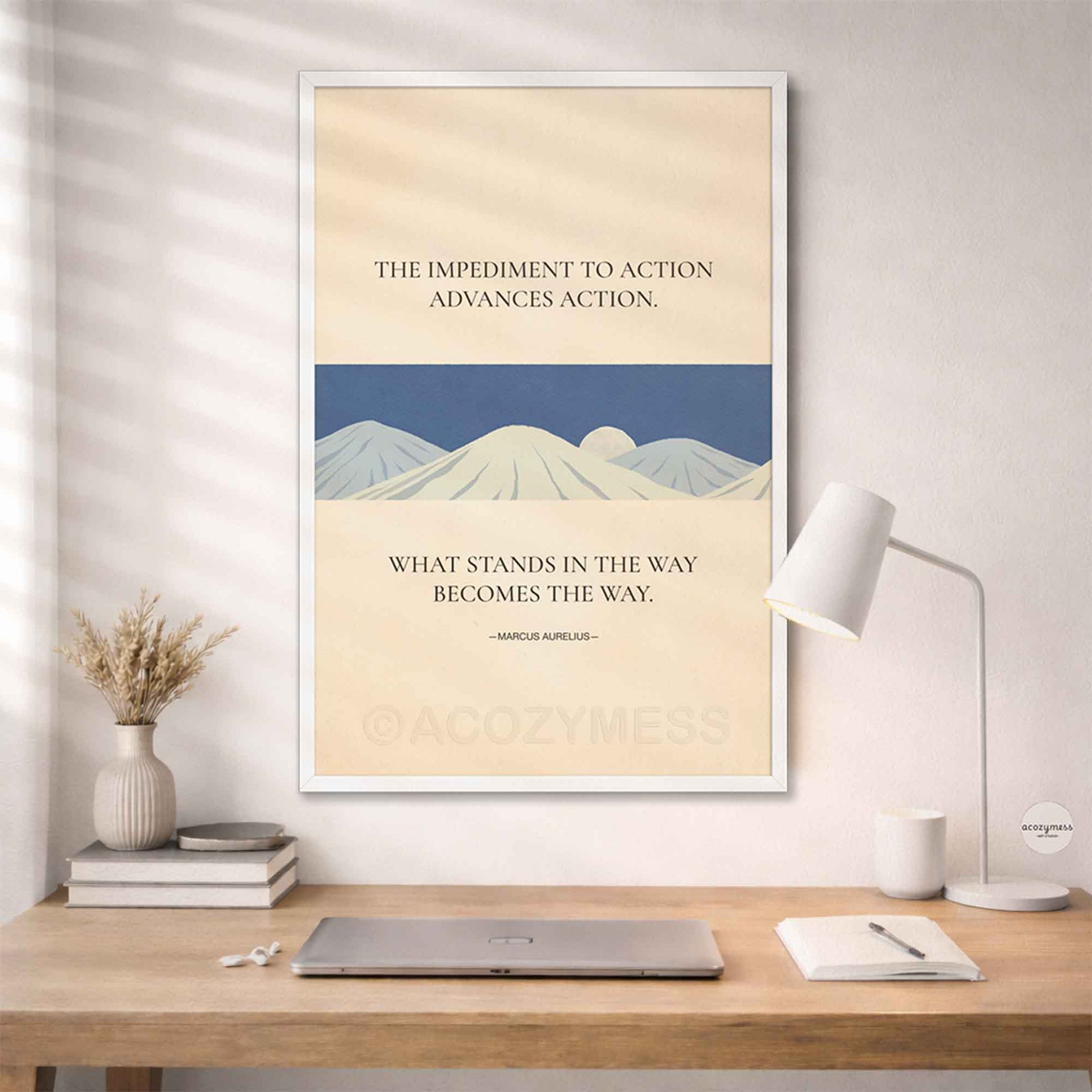White Framed motivational poster with mountain design and quote on a wall above a desk.