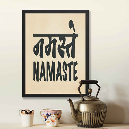 A black-framed typography poster featuring the word Namaste in both Hindi (नमस्ते) and English, displayed in bold black font on a beige background on a spiritual yoga wall.
