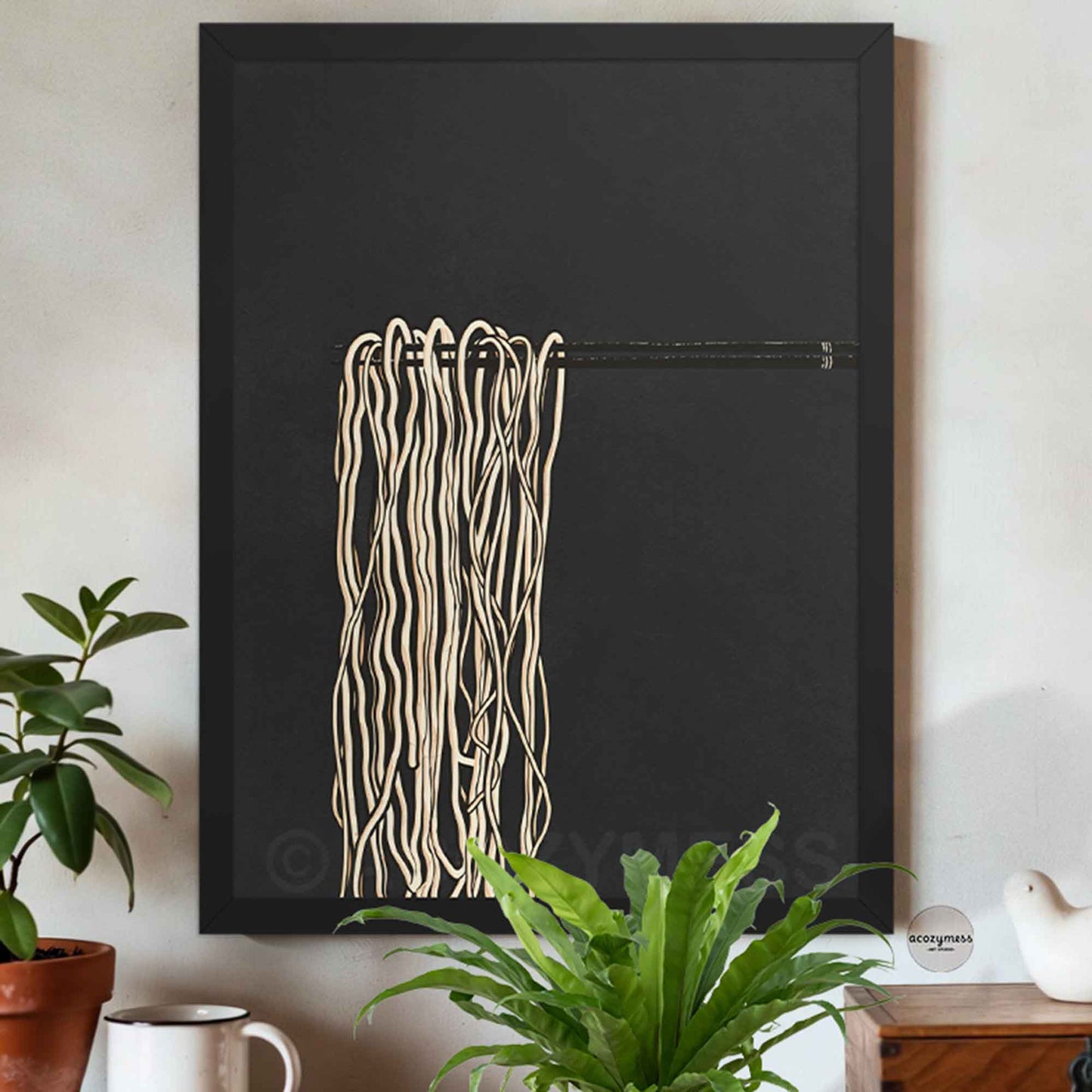 Black Framed abstract artwork with ramen noodles  art  on a black background, placed on a wall with plants and decor.