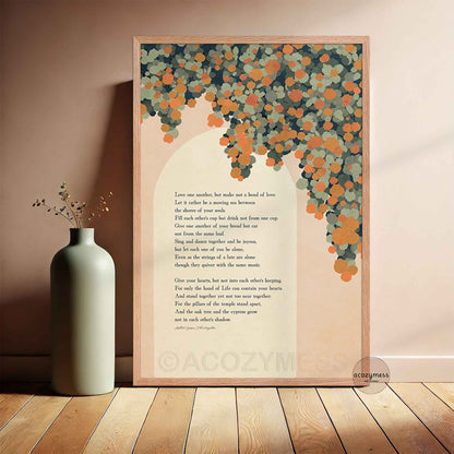 A framed vertical art print leaning against a beige wall, The print features a poem with a decorative background of orange florals on a cream backdrop, enclosed in a light wood frame.