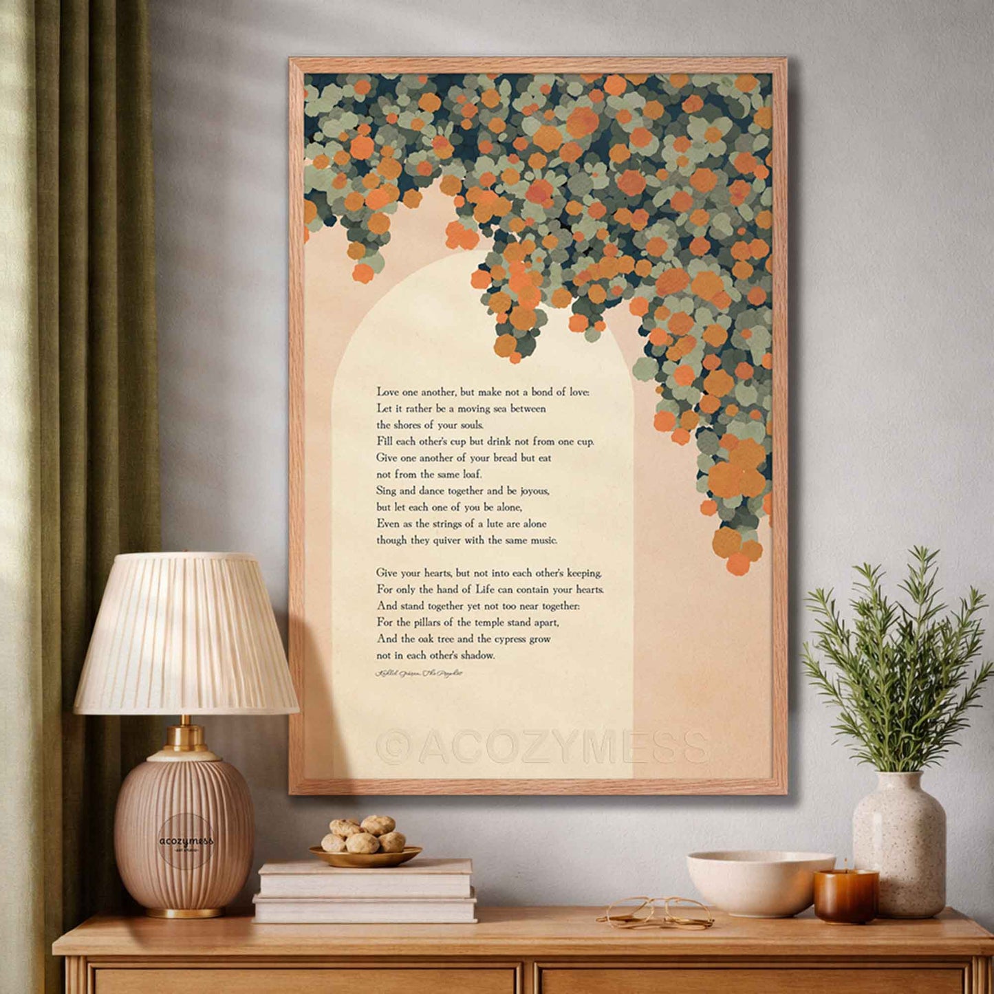 A framed wall art print featuring a poem on marriage with a peach background and a tree made of orange and teal leaves, displayed in a styled room above a wooden console table.