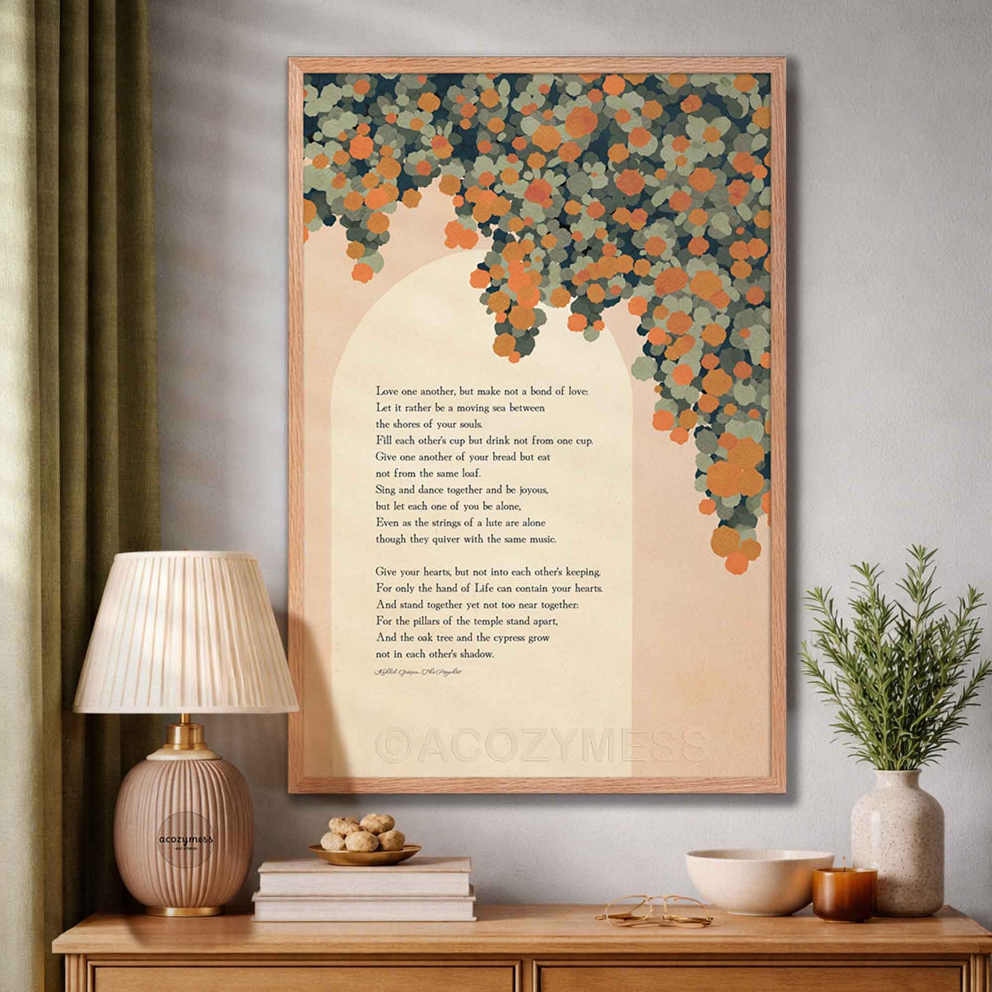 A framed wall art print featuring a poem on marriage with a peach background and a tree made of orange and teal leaves, displayed in a styled room above a wooden console table.