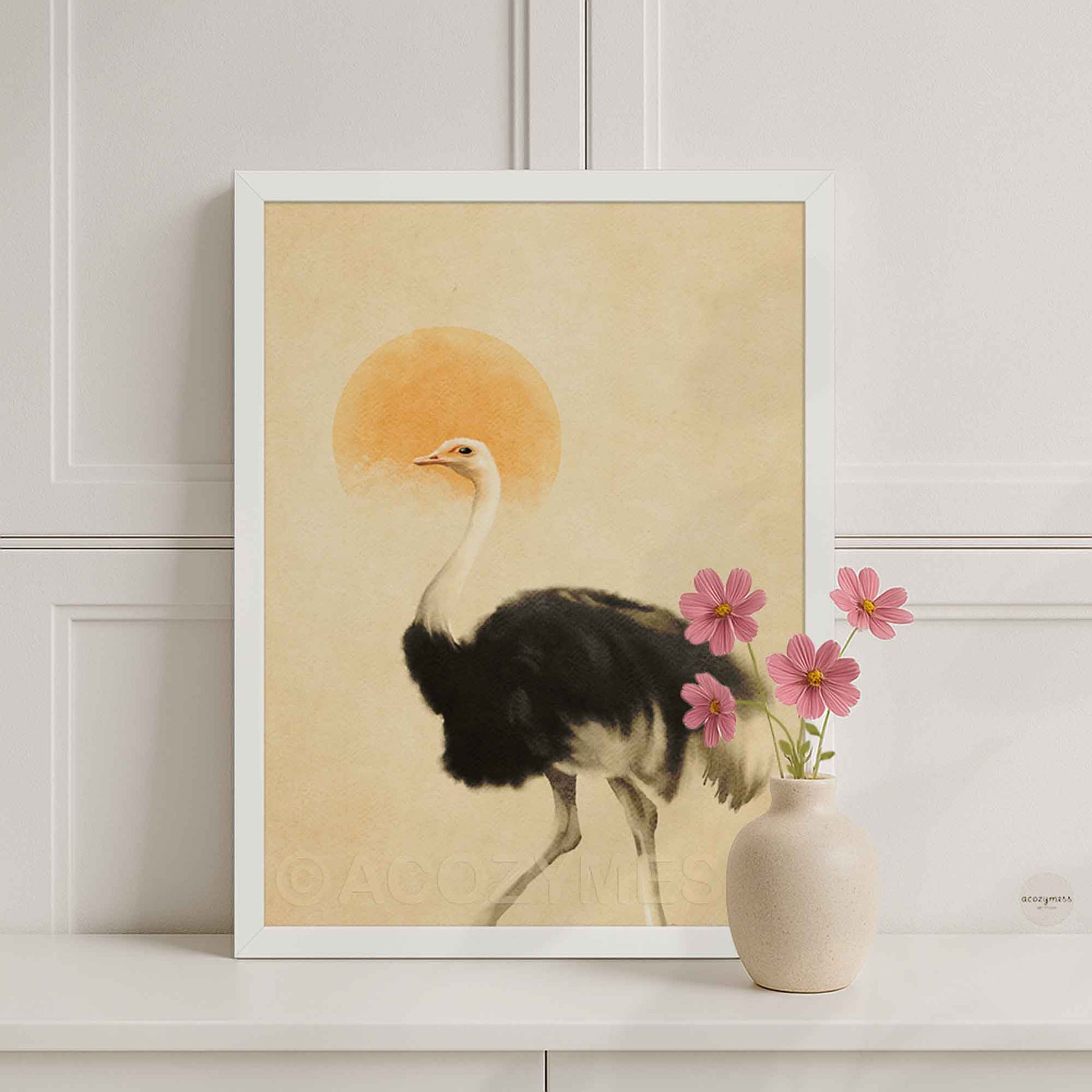 A framed art print featuring a black-and-white ostrich walking in front of a warm beige background with a soft orange sun, styled on a white shelf.