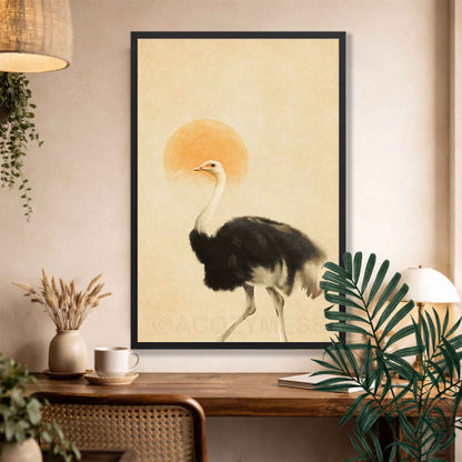 A framed art print featuring a black and white ostrich walking in front of a warm orange sun on a beige background, displayed on a wall above a wooden console table with plants and home decor.