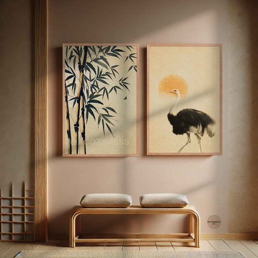 Two framed vertical art prints hang on a beige wall above a wooden bench. The left print shows dark bamboo on a cream background, and the right print shows a black-and-white ostrich with a warm orange sun.