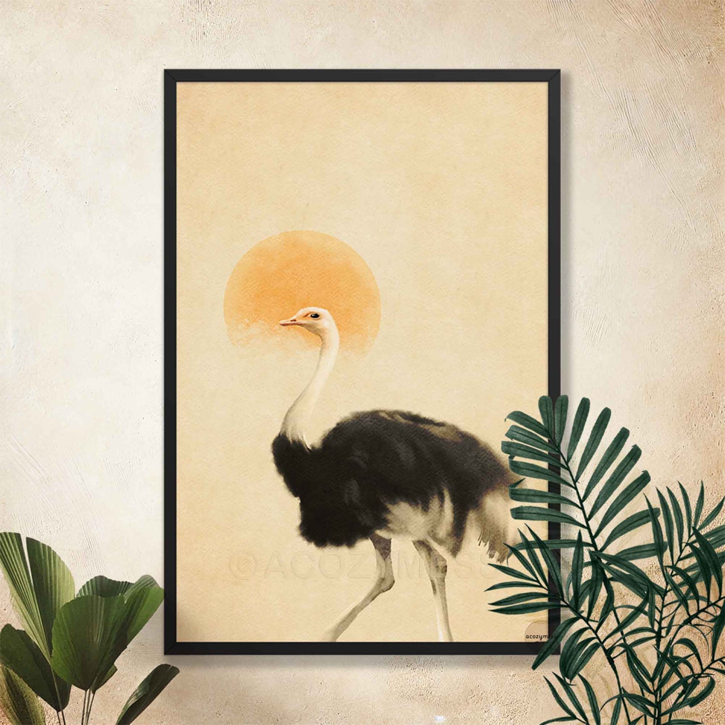 A framed art print featuring a black and white ostrich walking in front of a warm beige background with a soft orange sun, displayed on a textured beige wall with decorative green leaves.