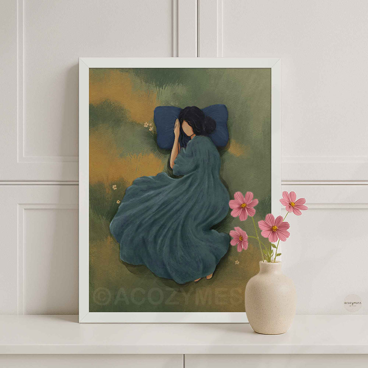 Minimalist white framed art poster of a woman sleeping peacefully in a green grassy meadow with a blue pillow, styled in a bright, calm interior setting.