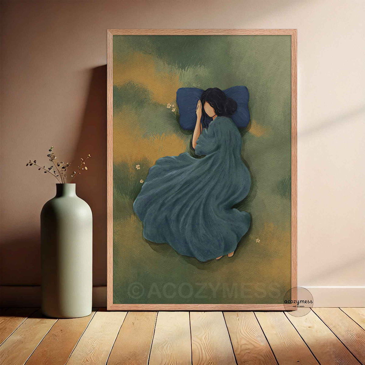 Resting woman in a meadow art print displayed in a light oak natural wood frame, leaning against a neutral wall