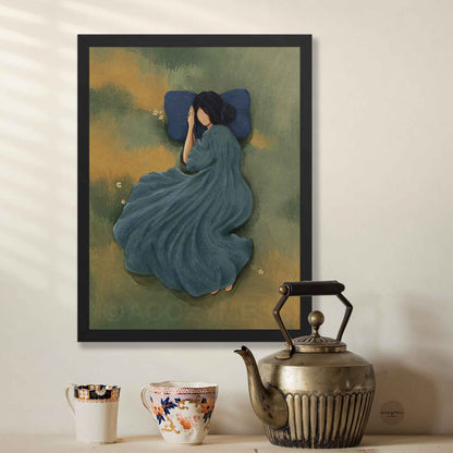 Black framed art poster of a woman sleeping peacefully in a green grassy meadow with a blue pillow, styled in a bright, calm interior setting.