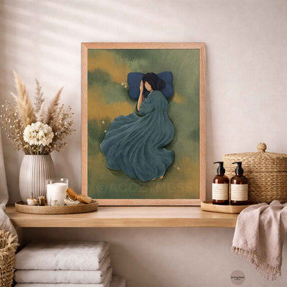 Natural wood framed art poster of a woman sleeping peacefully in a green grassy meadow with a blue pillow, styled in a bright, calm bathroom interior setting.