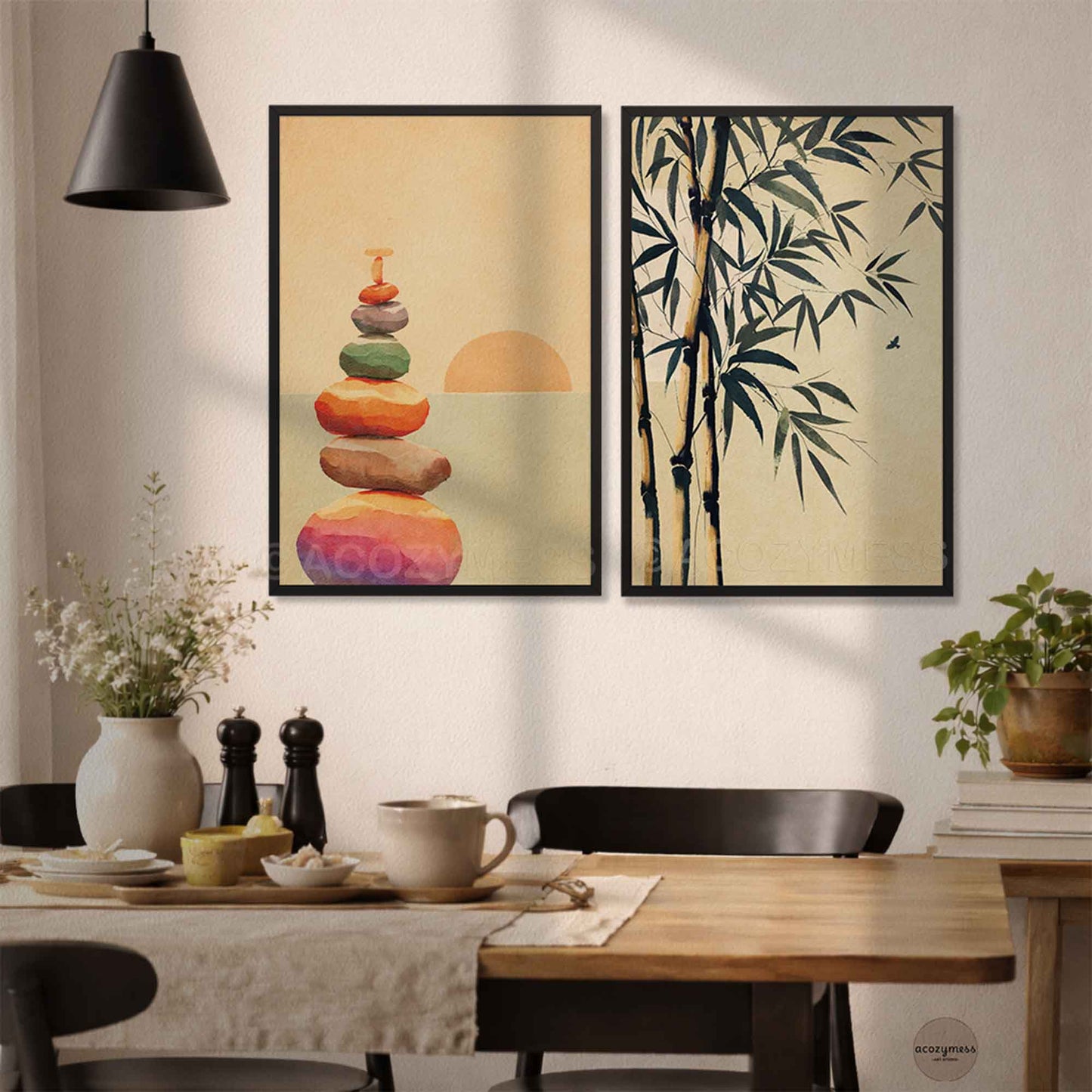 Two framed wall art prints hang above a dining table in a real interior setting. The left print shows stacked colorful stones with a sun motif on a warm beige background, and the right print shows  bamboo branches on the same beige background.