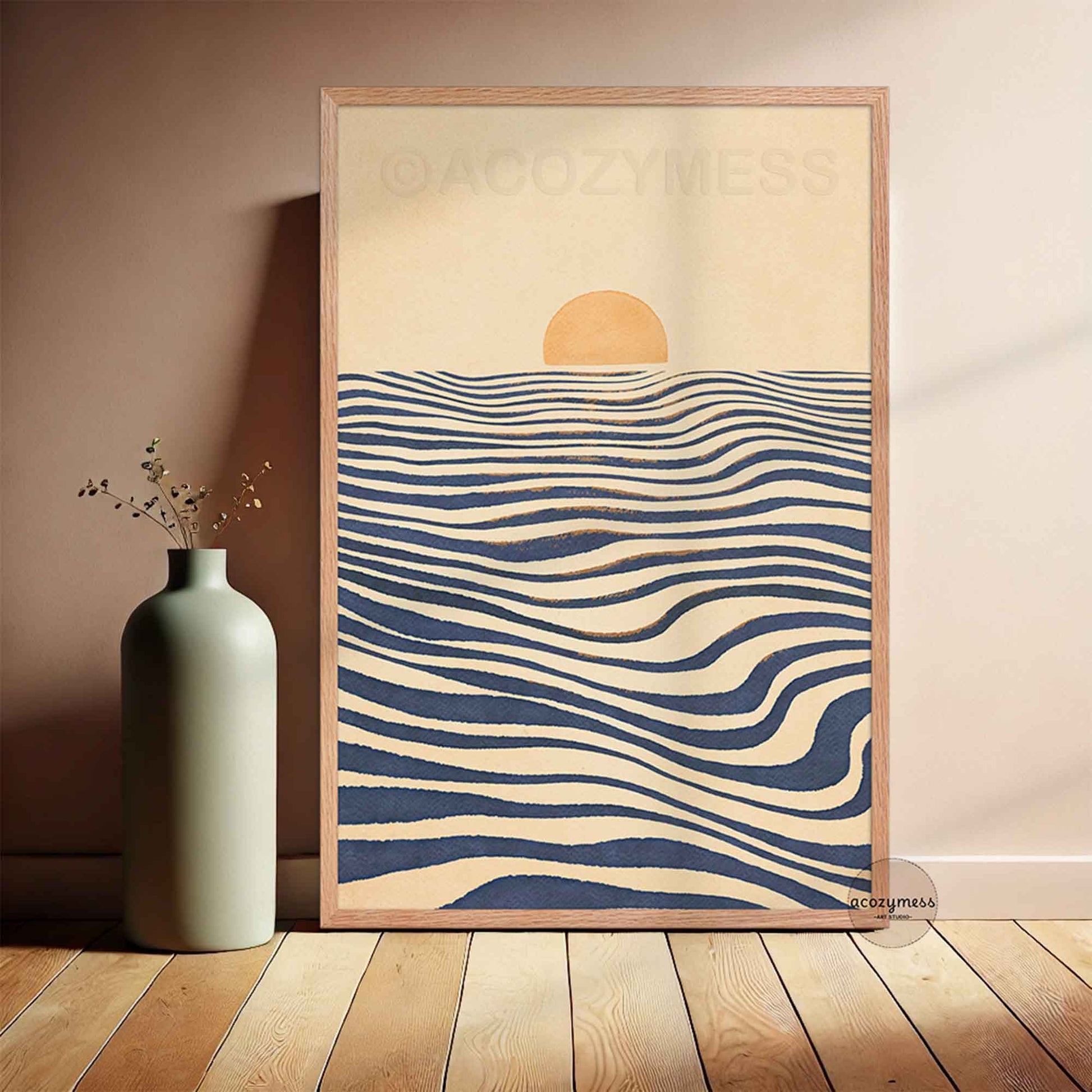 A wooden framed art print leaning against a wall on a wooden floor. The print features a minimalist design with a beige background, a small yellow sun, and wavy navy blue and beige horizontal lines resembling water.