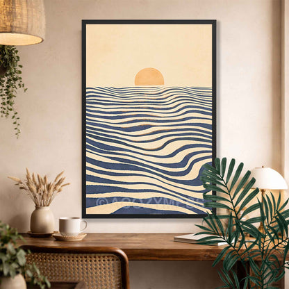 A framed wall art print hangs on a beige wall above a wooden table in a styled interior. The artwork shows a minimalist sunset scene with a pale yellow sun over cream and navy wavy horizontal lines, representing water.