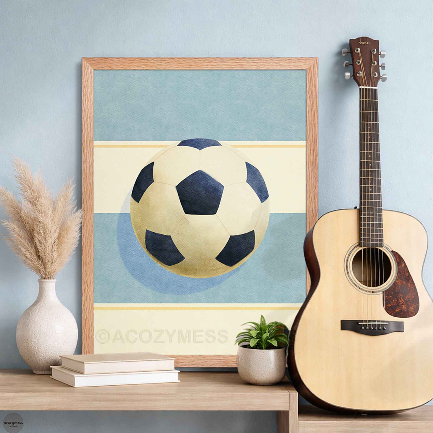 Soccer ball poster in an oakwood frame, clean sports artwork on soft light blue and beige tones.