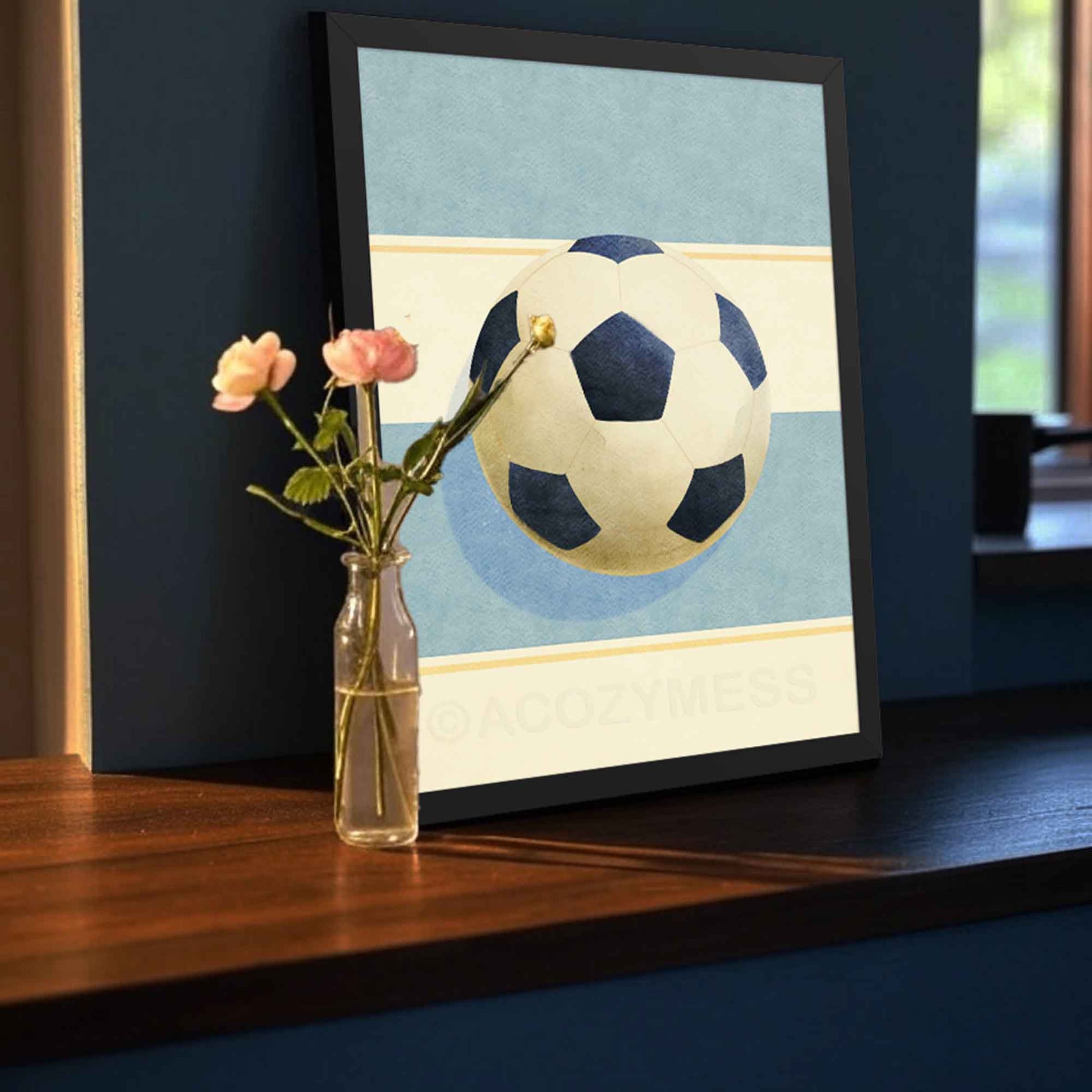 Soccer ball print in a black frame, high-contrast modern wall art on soft light blue and beige tones.