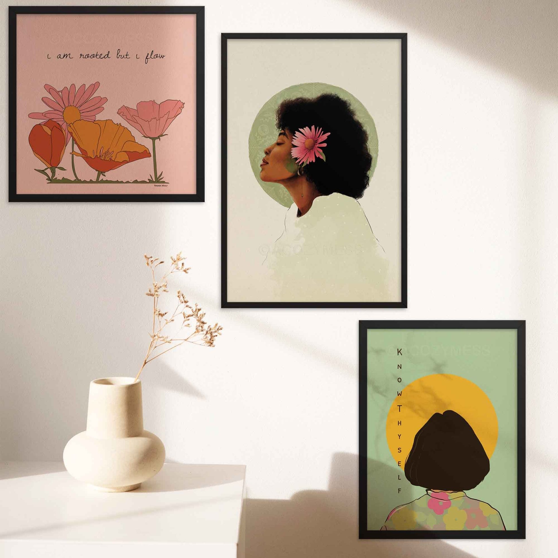 "Square art print featuring Virginia Woolf's quote 'I am rooted, but I flow,' with a vibrant floral illustration in pink, orange, and yellow hues. Displayed alongside a Black Woman Portrait art print and a 'Know Thyself' art print, all three elegantly framed in black on a wall."