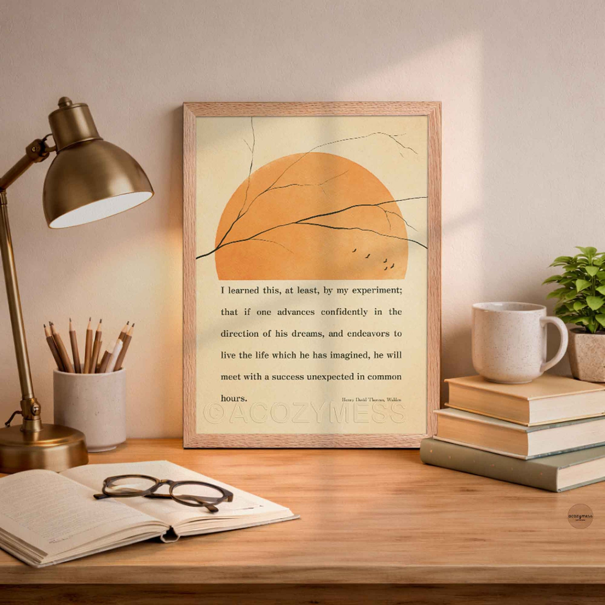 Inspirational Thoreau poster framed in oakwood with minimalist nature elements on beige background on a desk with lamp, books, and mug.
